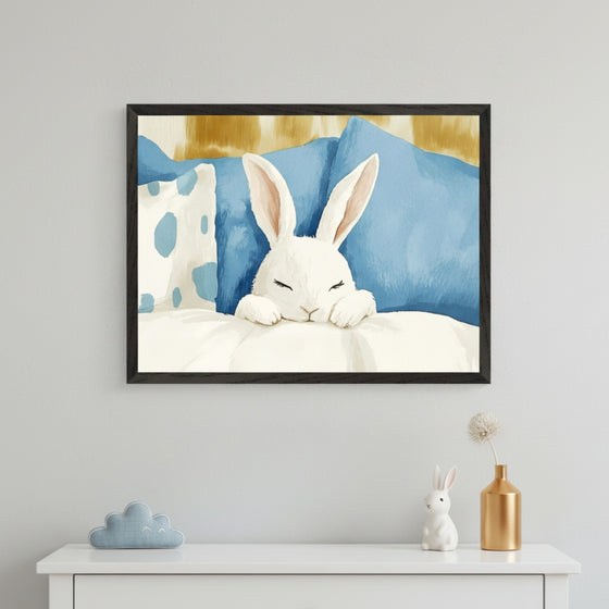 Kid's bedroom with a white dresser against a light gray wall. A framed watercolor painting of a white bunny sleeping in blue and white bedding hangs centered above the dresser. A blue cloud and white bunny figurine decorate the dresser.