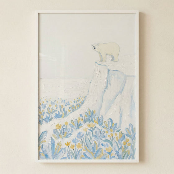 Framed painting of a polar bear standing on an icy cliff above a field of soft blue and yellow flowers in a minimal snowy landscape. The light textured brushstrokes and muted palette create a calm airy focal point against a neutral wall.