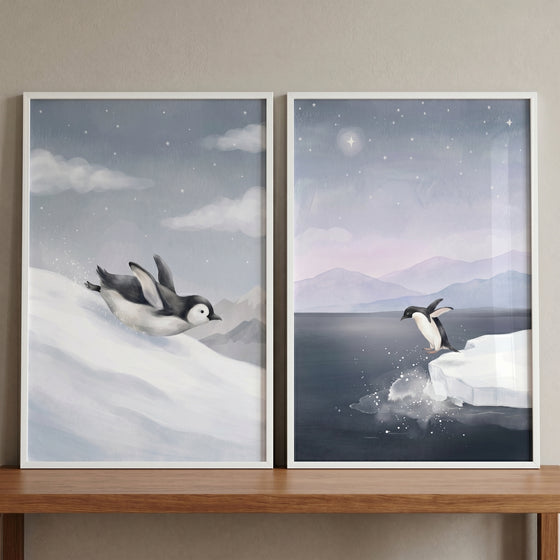Arctic starry night penguin wall art set of 2 shows a penguin sliding down snow and another jumping into water from ice.