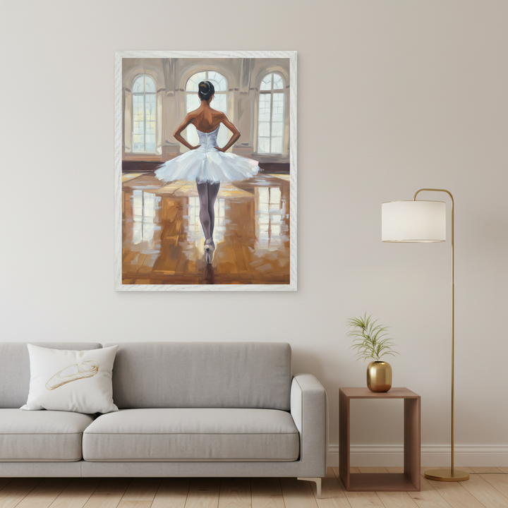 Modern living room with a gray sofa and a pillow with a ballet slipper. A large framed painting of a ballet dancer in a white tutu, seen from behind in a brightly lit studio with arched windows, hangs above the sofa. A wooden side table with a plant and a gold floor lamp are to the right.