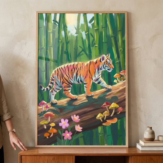 A vertical framed artwork featuring a young tiger cub with vibrant orange and black stripes. The cub is depicted walking across a large, dark brown fallen log. From the log, various colorful mushrooms in shades of yellow, red, and orange sprout, and small pink flowers bloom near its base.