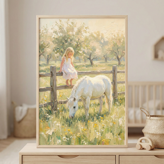 A framed impressionist painting of a young girl in a white dress sitting on a wooden fence while a white pony grazes in a sunlit meadow filled with wildflowers and soft green grass. The artwork rests on a light wood dresser in a neutral nursery setting, adding a gentle countryside storybook feel to the calm space.