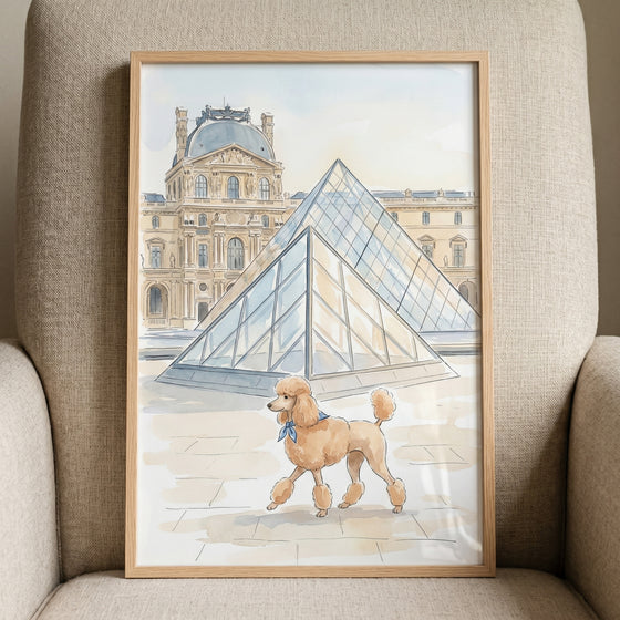 Blue scarf apricot poodle wall art shows a dog walking past a glass pyramid and historic palace in a light wood frame.