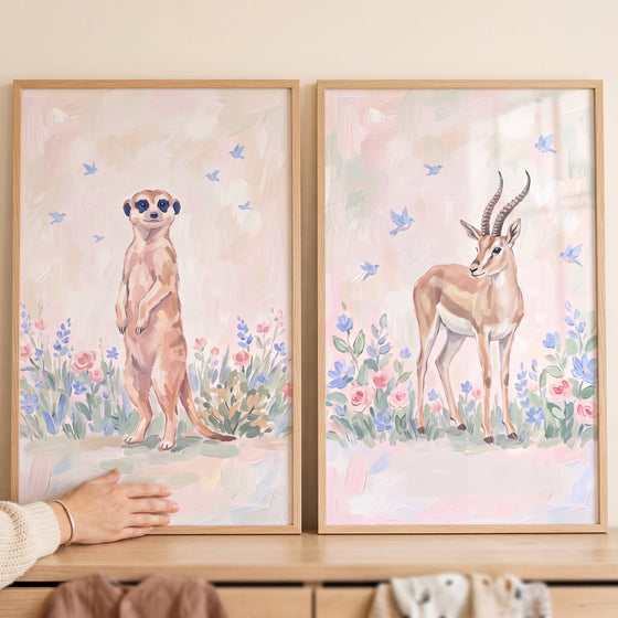 Blush bird safari animals wall art set of 2 with a meerkat and gazelle surrounded by flowers and blue birds.