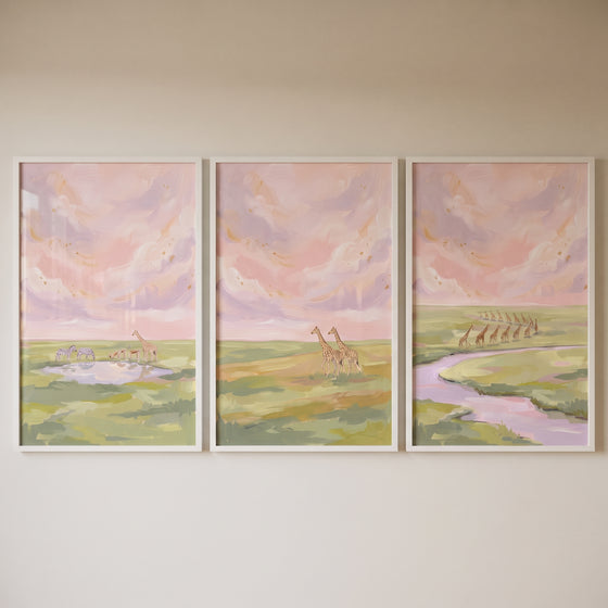 Blush pink savanna giraffe wall art set of 3 depicts animals by a watering hole and river under a soft pink sky.