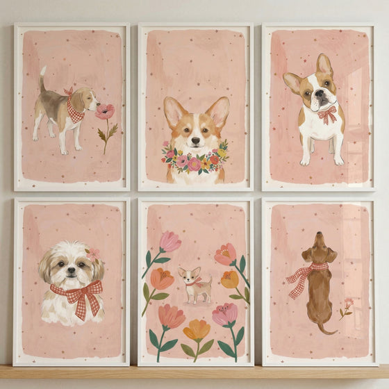 A vertical shot of a gallery wall displays six white-framed illustrations of various dogs arranged in a two-by-three grid. Each piece features a soft pink background with subtle speckles. The top row includes a beagle sniffing a flower, a corgi with a floral wreath, and a French bulldog with a bow tie.