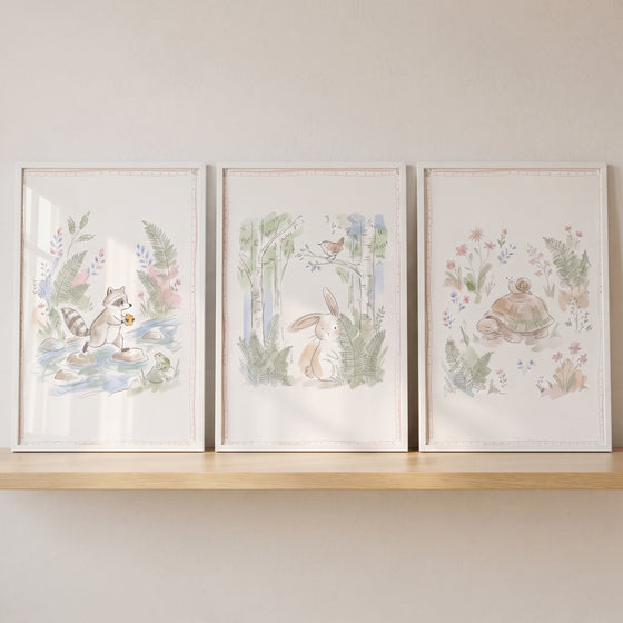 Botanical storybook forest creature artwork set of 3 on a shelf featuring a raccoon, bunny, turtle, and snail.