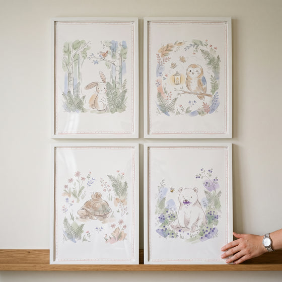 A dainty watercolor woodland animals wall art set of 4 featuring a bunny, owl, turtle, and bear in white frames.