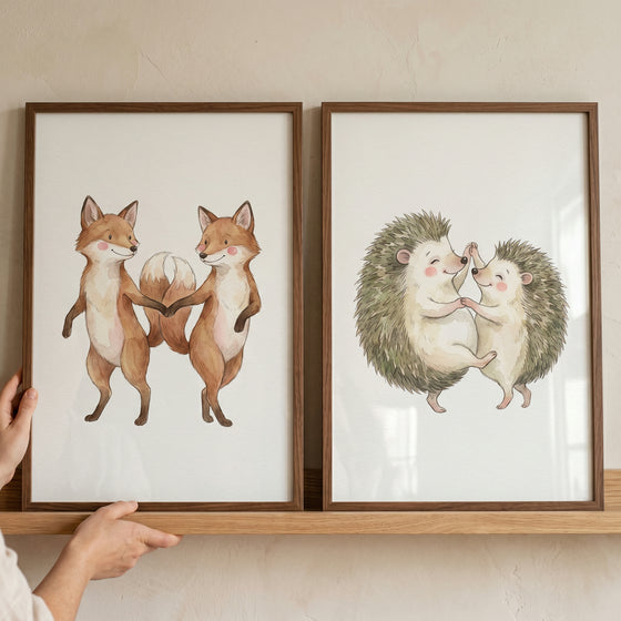 Dancing woodland animal wall art set of 2 featuring watercolor foxes and hedgehogs in frames on a wooden shelf.
