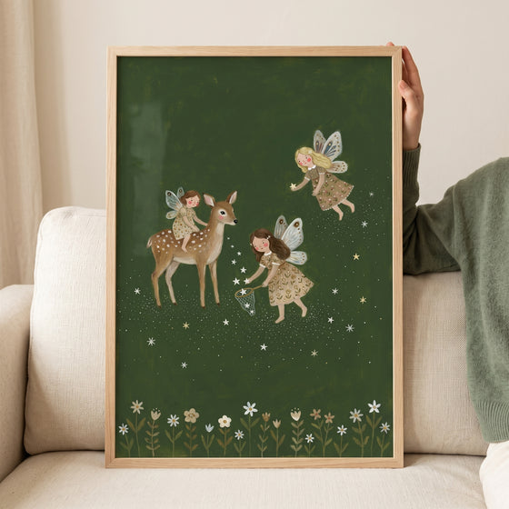 Dark green forest fairies wall art depicts three fairies and a deer catching stars above a row of white flowers.