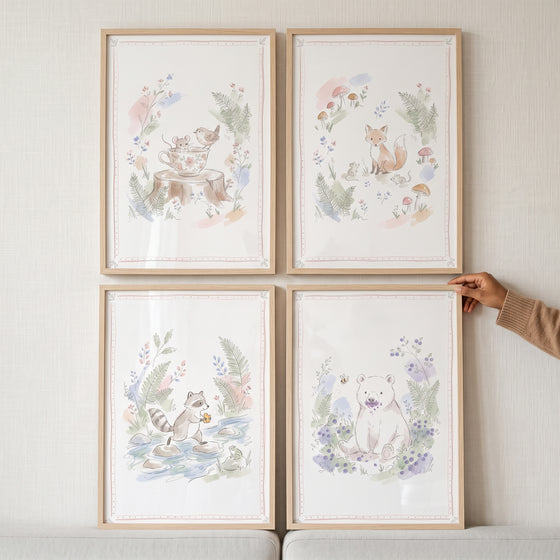 Hand holds a delicate botanical forest creature wall art set of 4, featuring a mouse, fox, raccoon, and bear in watercolor.