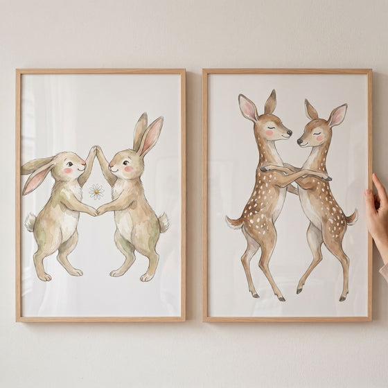 Delicate dancing woodland animal wall art set of 2 with watercolor rabbits and fawns in light wood frames.