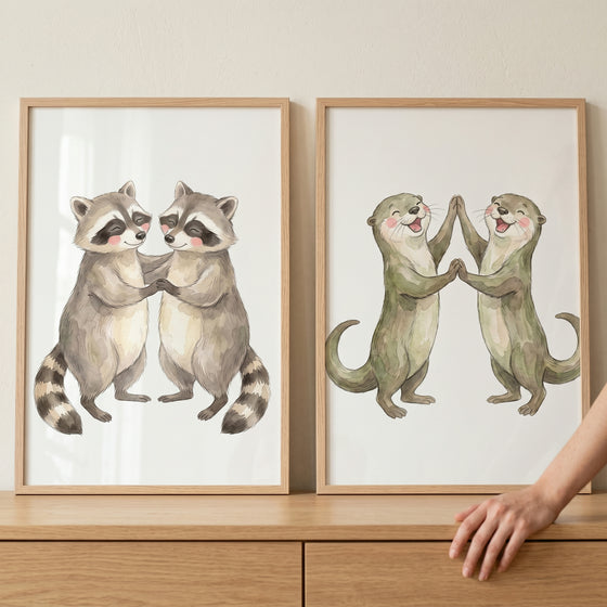 Earthy tone woodland animal print set of 2 shows raccoons holding paws and otters high-fiving in light wood frames.