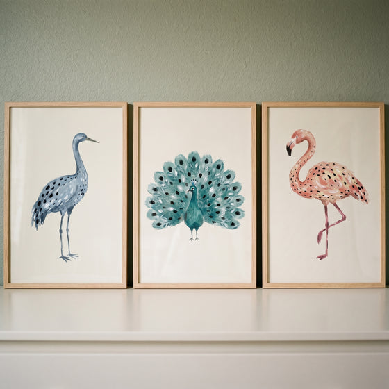 earthy watercolor spotted birds wall art set of 3 featuring a blue crane, teal peacock, and pink flamingo in wood frames.