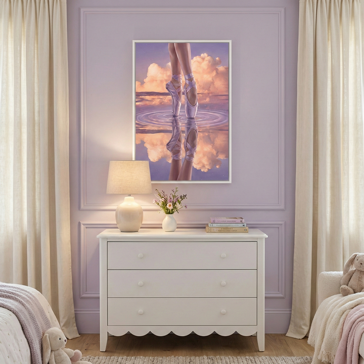 A serene and whimsically decorated room features a soft lavender wall with classic decorative molding. Centered on the wall is a piece of framed artwork showing a dancer’s feet in pointe shoes, poised on a reflective surface that mirrors a vibrant sunset with fluffy, glowing clouds.