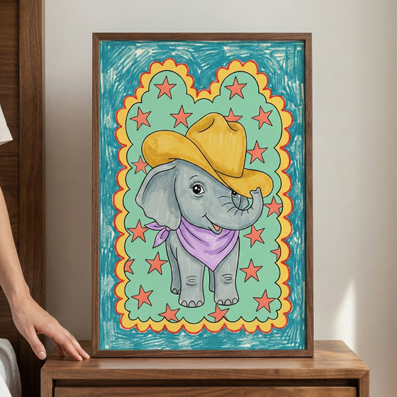 Framed drawing of a smiling cartoon elephant wearing a yellow cowboy hat and purple bandana, surrounded by red stars and a scalloped yellow and red border on a teal background, held by a person next to a wooden bed frame.