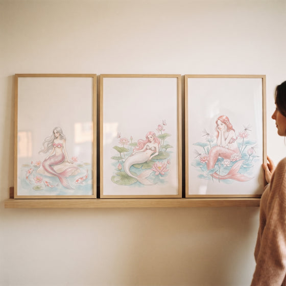 A feminine aquatic botanical mermaid artwork set of 3 displayed in wooden frames on a light wood floating shelf.
