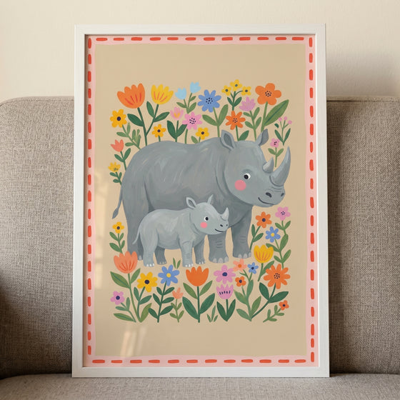 Folk floral garden rhino wall art with two grey rhinos among colorful flowers in a white frame on a grey couch.