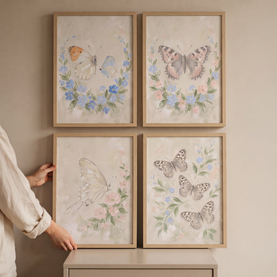 A person displays a four piece meadow butterfly wall art set of 4 with pastel insects and flowers in light wood frames.