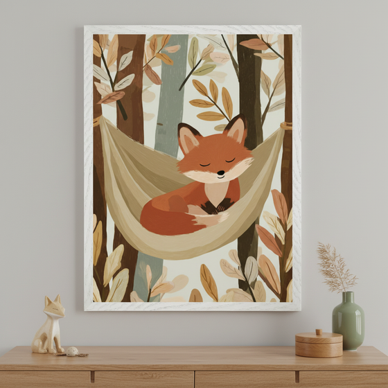 Framed illustration of a sleeping fox curled up in a beige hammock, hanging between trees with muted autumn leaves in soft tones. The artwork is displayed above a wooden dresser, decorated with a ceramic fox figurine and minimalist home decor.