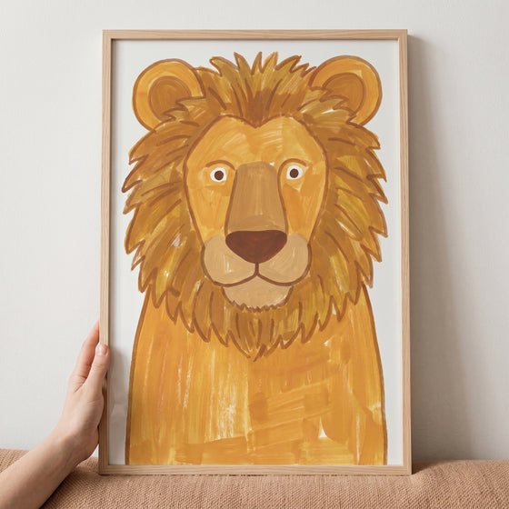 Hand holding a light wood frame with a friendly lion illustration, golden lion wall art.