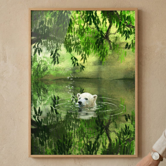 A framed digital illustration hangs on a textured, light beige wall. The scene depicts a white bear's head emerging from a still, green pool of water. Small ripples and bubbles surround its snout. Lush green foliage and overhanging leaves fill the upper portion, their vibrant shades reflected on the water below. The artwork utilizes textured brushwork for a soft, layered effect. It is enclosed in a slim, light-wood frame. A person's wrist with a watch is visible in the bottom right corner.