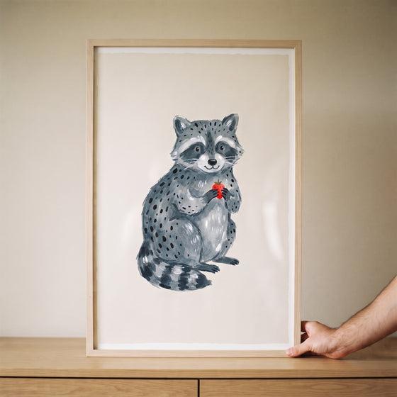 Framed holding strawberry grey raccoon wall art on a wooden surface, supported by a hand against a neutral background.