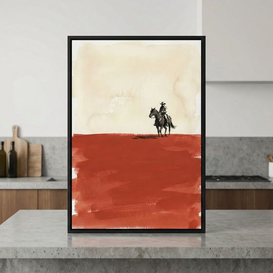 Framed artwork of a cowboy on horseback set against a stark desert landscape with a beige sky and deep red foreground, displayed on a modern kitchen island. The western-style illustration uses bold, minimalist brushstrokes to emphasize solitude and open space.