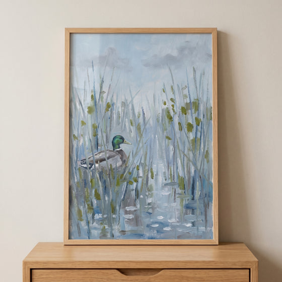 Framed impressionist marshland mallard duck wall art sits on a wood dresser, showing a bird in a blue wetland scene.