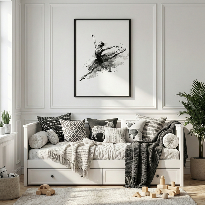 A bright, minimalist room features a white daybed set against a wall with classic panel molding. Centered above the bed is a large, black-framed monochromatic artwork of a dancer performing a graceful mid-air leap, styled with fluid, ink-like strokes. The bed is layered with textured blankets and patterned pillows in black, white, and grey. To the right stands a tall, leafy potted plant, and simple wooden toys are scattered on a plush white rug covering the light wood floor.