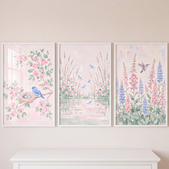 Light pink botanical wall art set of 3 with a bluebird, dragonflies by water, and a hummingbird among tall flowers.