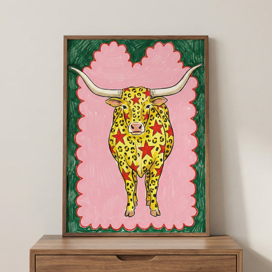 Colorful illustration of a longhorn cow with yellow and red star-leopard spots, set against a pink background with a green and red border.