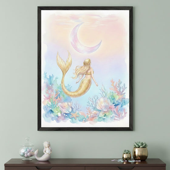 Modern kid's room with a dark wooden dresser against a sage green wall. A framed watercolor art print of a golden-tailed mermaid swimming among coral and shells towards a pastel moon hangs above. A mermaid figurine and a jar of candies are on the dresser.