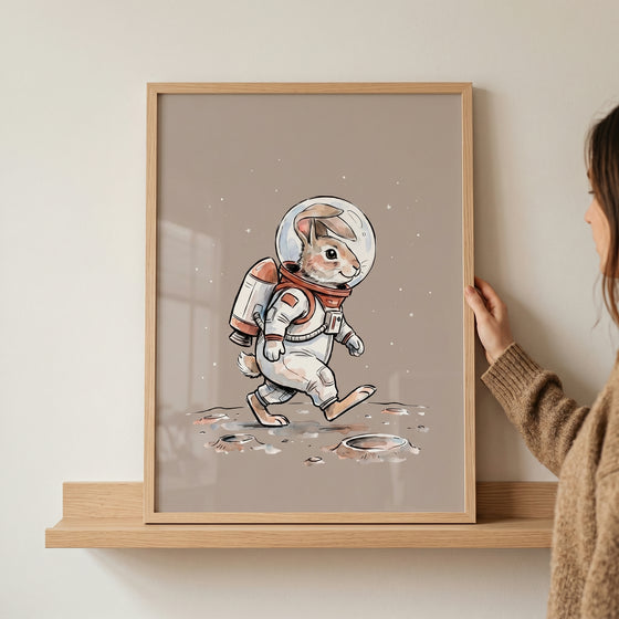 Framed moon walking astronaut bunny wall art featuring a rabbit in a space suit walking on a cratered moon surface.