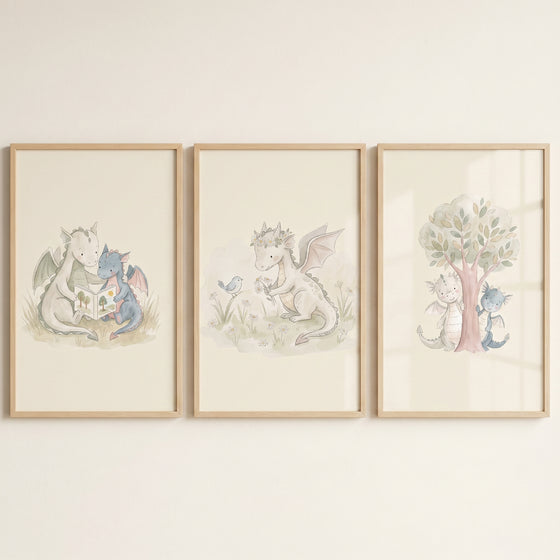 Muted cream baby dragons wall art set of 3 in wood frames depicting dragons reading, playing with a bird, and by a tree.