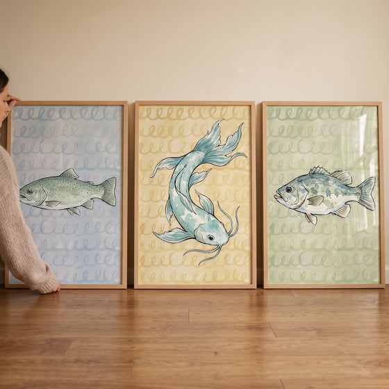Muted watercolor sketchy fish wall art set of 3 in light wood frames held against a wall on a wooden floor.