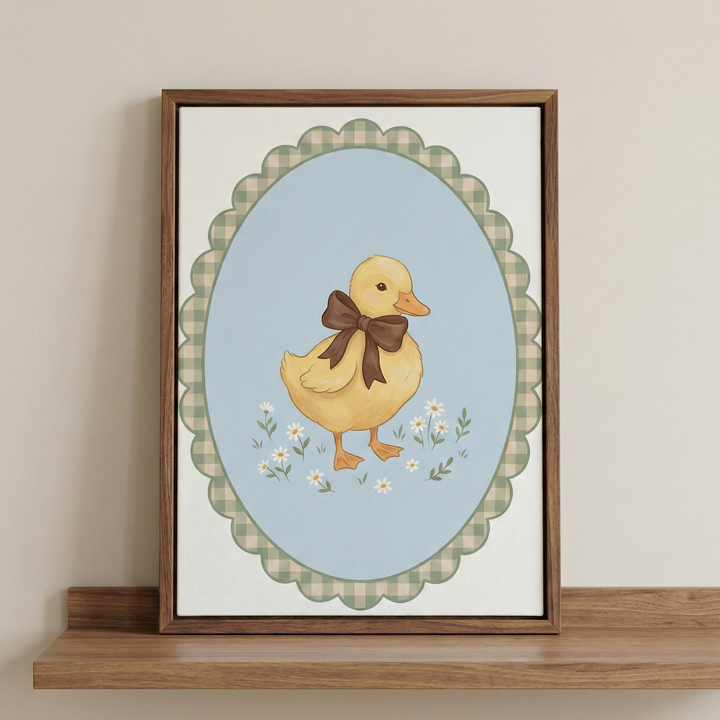 A sweet nursery-style illustration featuring a soft yellow duckling adorned with a large brown bow. The duckling stands among tiny white daisies set against a light blue oval backdrop. Encircling the oval is a decorative scalloped border with a green and cream gingham pattern. This artwork is displayed in a dark brown wooden frame, resting on a simple wooden shelf against a plain, warm-toned wall.