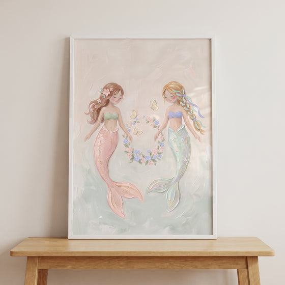 Pastel floral wreath mermaid wall art featuring two mermaids with colorful tails in a white frame on a wooden table.