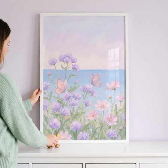 Framed pastel purple floral butterfly wall art being positioned by a person above a white surface.