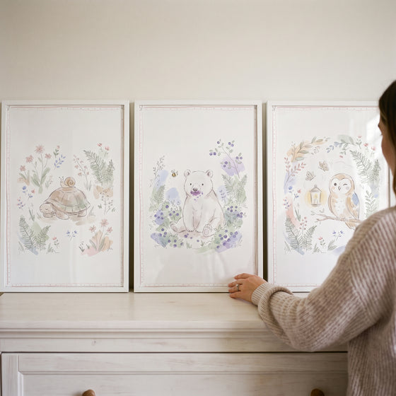 A woman arranges a pastel sketched forest animal wall art set of 3 featuring a turtle, bear, and owl on a white dresser.