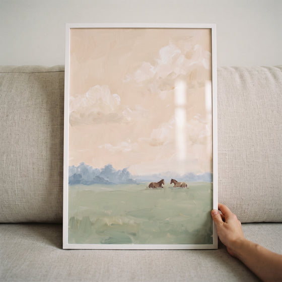Framed pastel sky resting horse print shows two brown horses in a green field under a soft peach sky with white clouds.