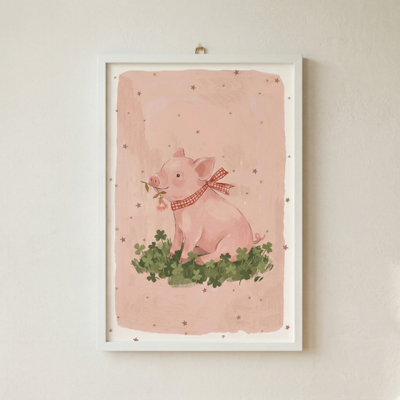 A whimsical illustration of a small, pink pig sitting on a bed of green clovers. The pig is shown with a gentle expression, holding a tiny sprig with a pink flower in its mouth. Around its neck is tied a red and white checkered ribbon. The backdrop is a soft pink, punctuated by small, brown star-like shapes. This artwork is housed in a clean white frame and hung on a neutral, textured wall.