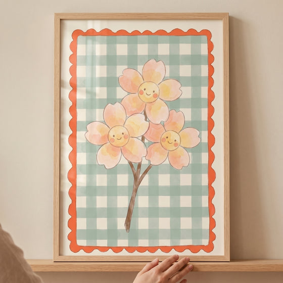 Pink smiley face flower wall art in a wood frame with three flowers, a green checkered background and orange scalloped.