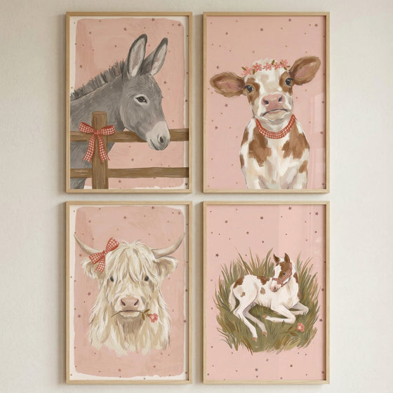 Four framed illustrations of farm animals are arranged in a square on a plain wall. Each piece features a soft pink background with delicate speckles. The top-left depicts a grey donkey behind a wooden fence adorned with a red checkered bow. To its right is a brown and white calf wearing a crown of flowers and a red necklace. Below, a fluffy white cow with horns sports a red checkered bow and holds a pink flower. The final image shows a small brown and white horse resting in tall grass.