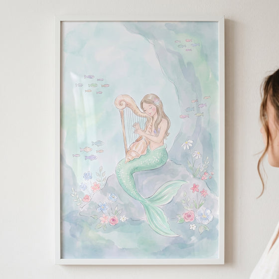 Watercolor playing harp mermaid wall art shows a mermaid on a rock with colorful sea flowers and swimming fish.