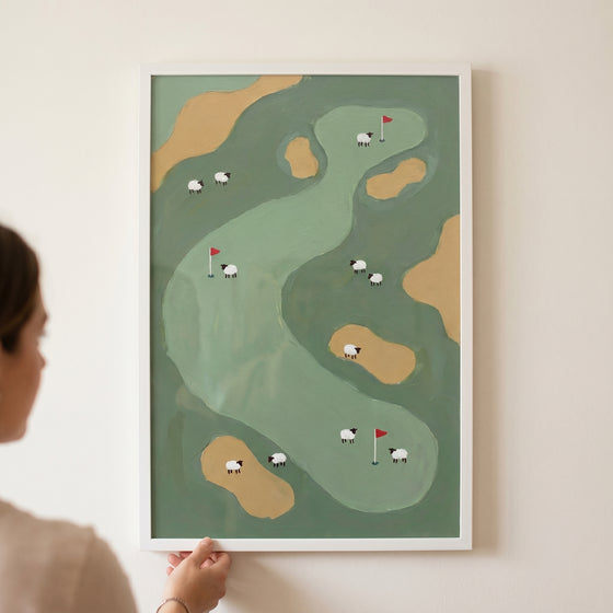 Framed red flag golf sheep wall art showing white sheep grazing on a green golf course with sand traps and red flags.