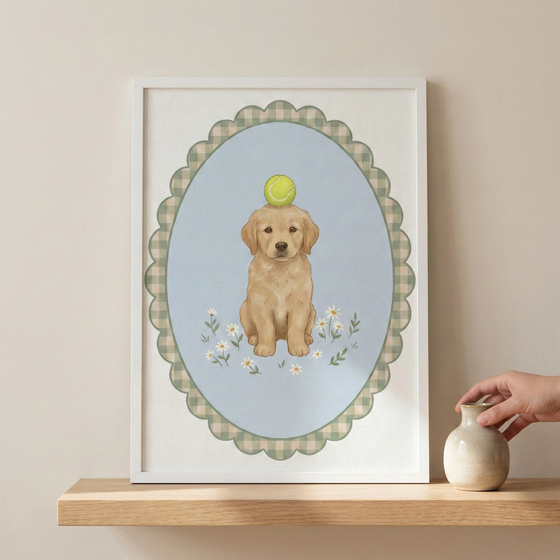 An illustration of a light brown puppy sitting patiently with a green tennis ball balanced on its head. The puppy is set against a light blue oval backdrop decorated with small white flowers. Surrounding the oval is a scalloped border with a green and white checkered pattern. The entire artwork is presented in a plain white frame, which sits on a wooden shelf next to a small, rounded ceramic vase.