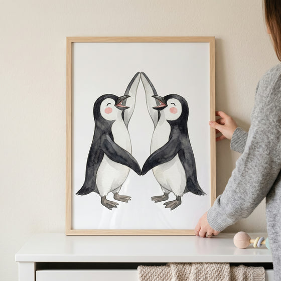 Two watercolor penguins touch flippers in this rosy cheek dancing penguin wall art held above a white dresser.