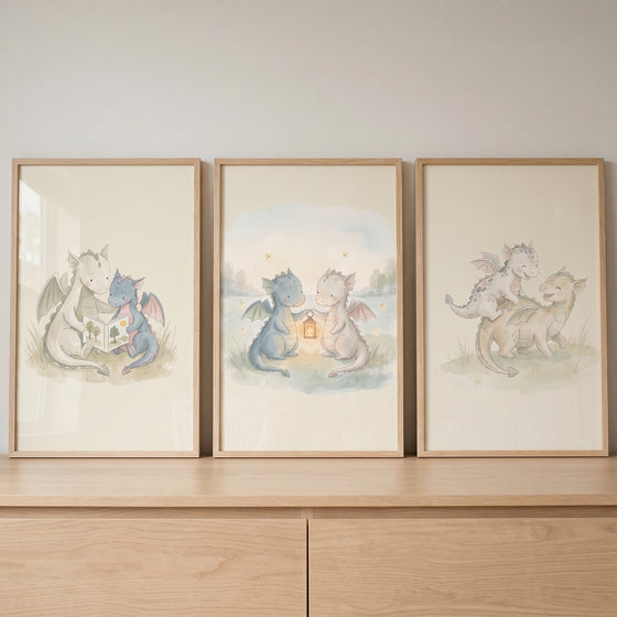 Sage cream baby dragons wall art set of 3 with watercolor scenes of dragons reading a book, holding a lantern, and playing.