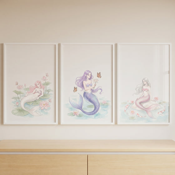 Serene pastel watercolor mermaid wall art set of 3 displayed in white frames on a wall above a light wood dresser.